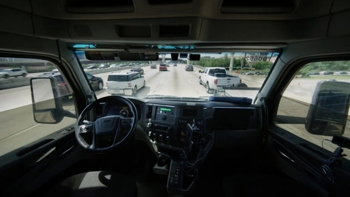 Interior view of an empty commercial truck cab driving on a multi-lane highway with no driver behind the wheel